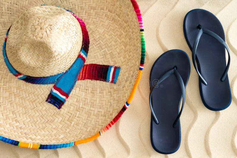 Straw sombrero and sandals on beach sand