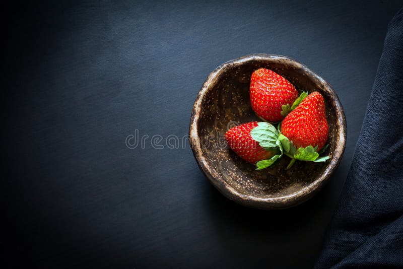 Strawberries in bowl on black background, table top view