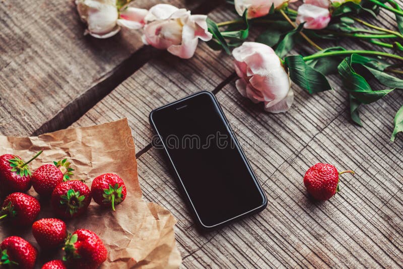 Strawberries, flowers and phone on the rustic table.