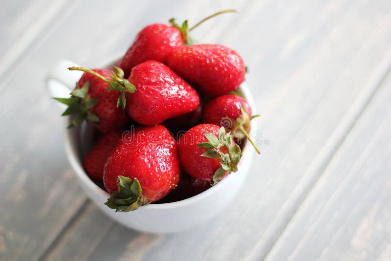 Strawberries in white cup on wooden grey desk.