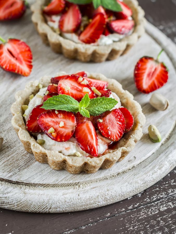 Strawberry tartlet with vanilla cream on a light rustic wooden board.