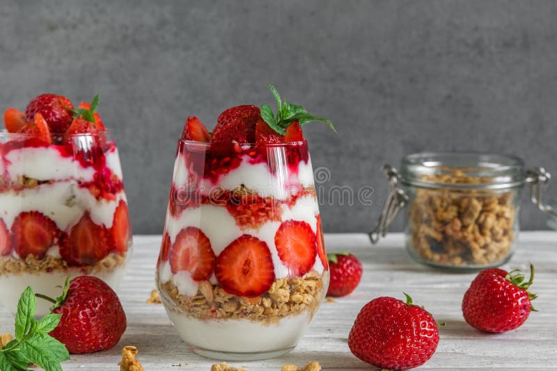 Strawberry yogurt parfait with granola, mint and fresh berries in glasses on white wooden table. healthy breakfast