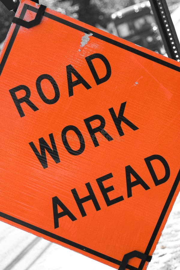 An orange road sign that reads ROAD WORK AHEAD. An orange road sign that reads ROAD WORK AHEAD