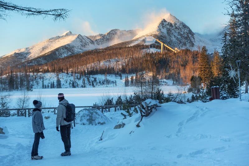 Unknown people standing near Strbske Pleso lake and looking far to the snowy mountain peaks of the High Tatras.