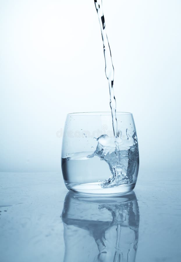 A stream of water flowing into a transparent glass cup with a splash of drops and drops. A jet of clean drinking spring water