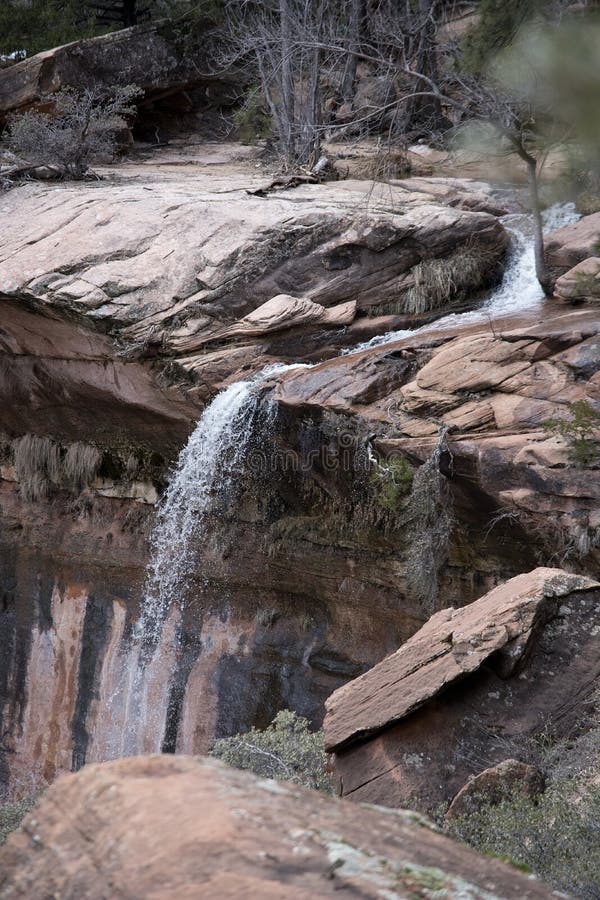 Stream and Waterfall Over Red Sandstone Cliffs with Branches in Winter royalty free stock photo Stream and Waterfall Over Red Sandstone Cliffs with Branches in Winter royalty free stock photo