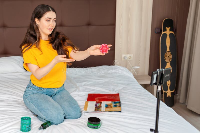 Streaming and vlogging. A beautiful female vlogger streaming live video on smartphone showing a cosmetics while sitting on a bed. Streaming and vlogging. A beautiful female vlogger streaming live video on smartphone showing a cosmetics while sitting on a bed.