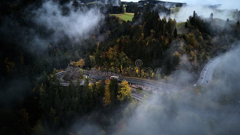 Street from above trough a misty forest at autumn, aerial view flying through the clouds with fog and trees