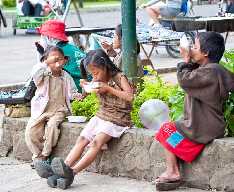 Filipino street children in a park in Baguio City, Philippines eating their meal in sidewalk of the street.