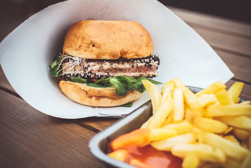 Street food. close up of fresh grilled tuna burger with on paper. wooden background