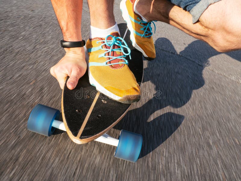 Street high-speed sports: A guy in yellow sneakers is rolling on a longboard along the road. Asphalt is smeared with