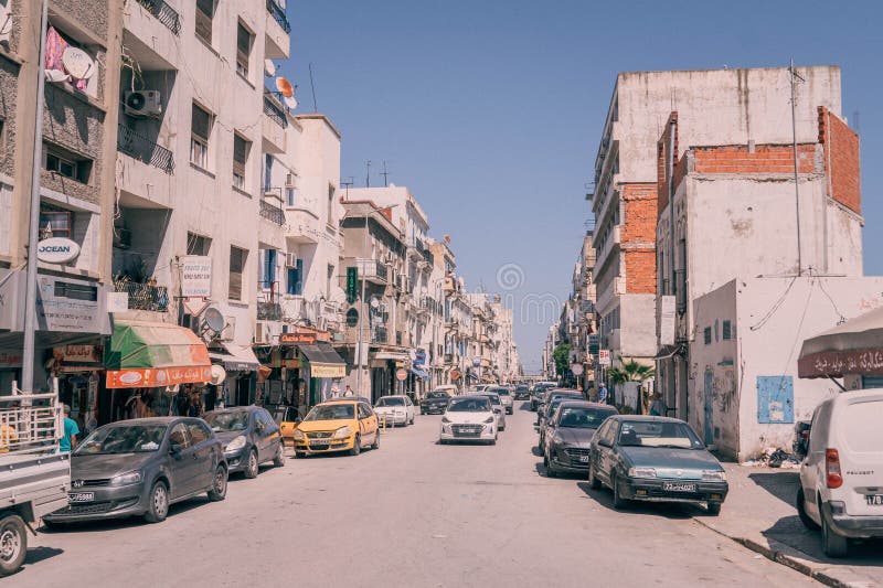The dusty narrow street with parked cars and old buildings in downtown of Tunis during the hot summer day in Tunisia. The dusty narrow street with parked cars and old buildings in downtown of Tunis during the hot summer day in Tunisia