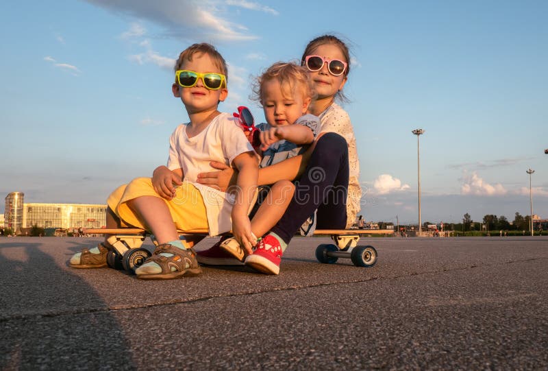 Street sports: A boy and two girls in sunglasses sit together on a large longboard. The summer solchechny frame.