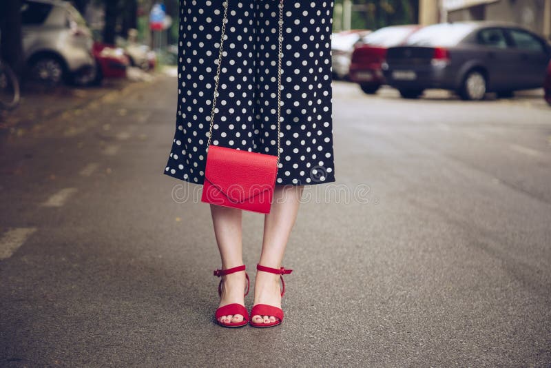 Stylish woman in polka dot culottes and denim jacket holding a red purse and wearing a rose gold wrist watch.