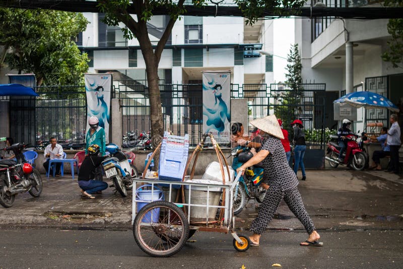 Street Vendor Pushing A Cart. A Vietnamese street vendor pushes a cart full of plastic stools and buckets on the streets of Ho Chi Minh City. She is wearing the royalty free stock images Street Vendor Pushing A Cart. A Vietnamese street vendor pushes a cart full of plastic stools and buckets on the streets of Ho Chi Minh City. She is wearing the royalty free stock images