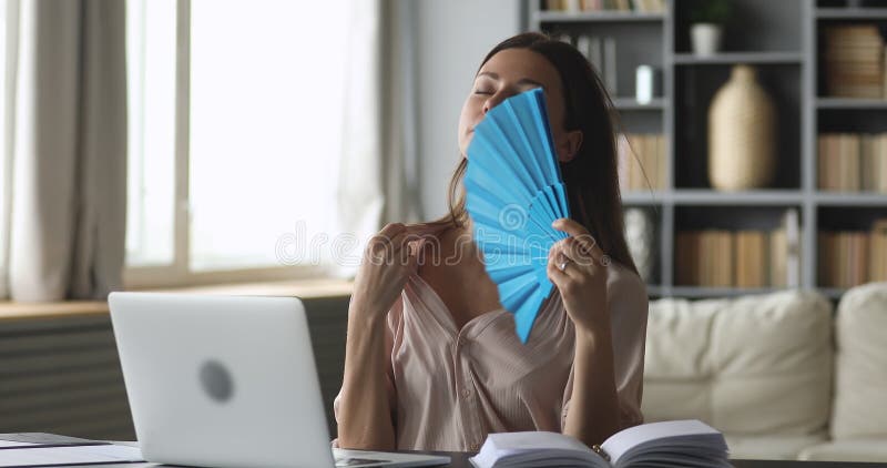 Stressad ung kvinna som använder fläkt som har hög temperatur inuti.