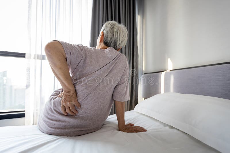 Stressed asian senior woman suffering from backache,sitting on bed massage her waist pain,unhappy old elderly people waking up in