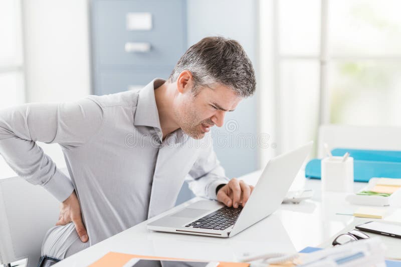 Stressed businessman with backache, he is working at office desk and massaging his back stock photography Stressed businessman with backache, he is working at office desk and massaging his back stock photography