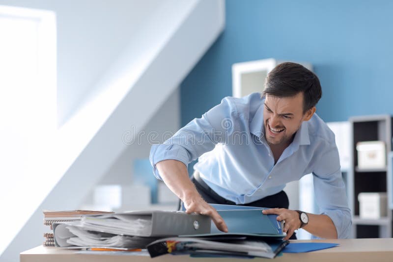 Stressed Businessman Sweeping Documents Off Table in Office Stock Photo