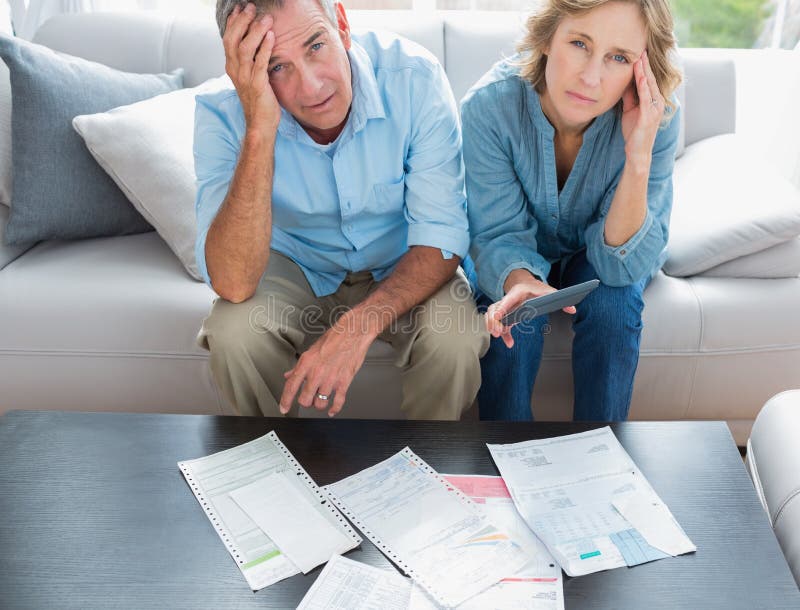 Stressed couple sitting on their couch paying their bills. Smiling at camera at home in the living room royalty free stock photography Stressed couple sitting on their couch paying their bills. Smiling at camera at home in the living room royalty free stock photography
