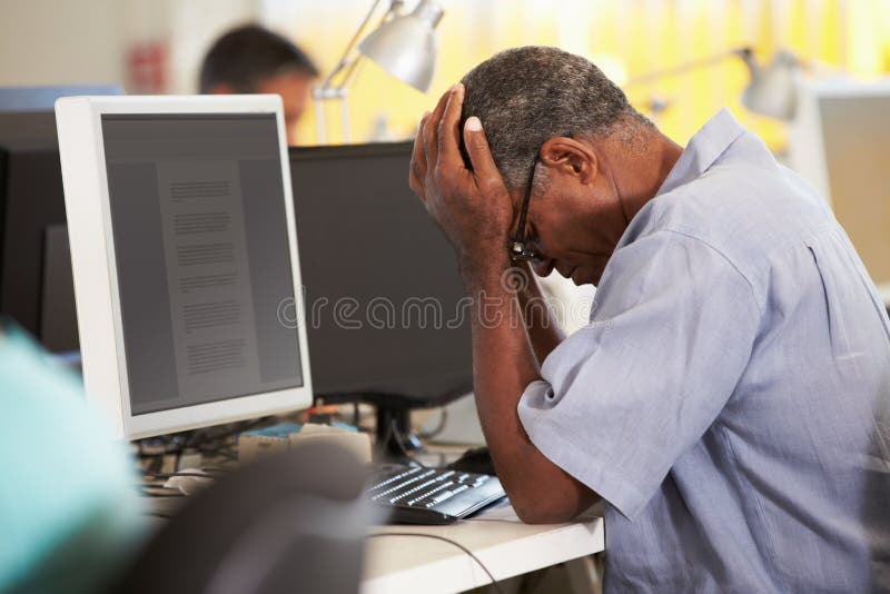 Stressed Man Working At Desk In Busy Creative Office On Computer