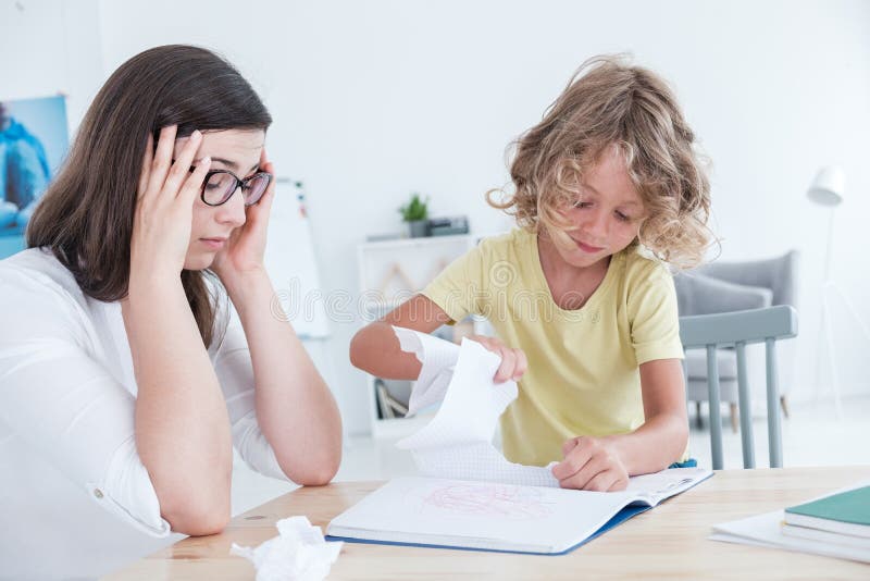 Stressed psychotherapist having a headache during a meeting with a rebellious child with behavioral disorders. The kid is tearing