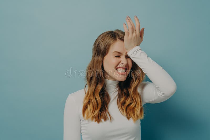 Stressful woman with brown hair wearing casual clothes holding hand on head having disappointment and stressful situation, looking frustrated with eyes closed isolated on blue with free space. Stressful woman with brown hair wearing casual clothes holding hand on head having disappointment and stressful situation, looking frustrated with eyes closed isolated on blue with free space