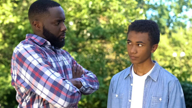 Strict black dad looking at guilty teenage son, upbringing methods, family. Stock photo royalty free stock photos
