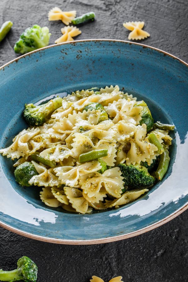Strikt vegetarianFarfalle pasta i en spenatsås med broccoli, brussels groddar, haricot vert i platta på mörkerstenbakgrund Top be royaltyfria bilder Strikt vegetarianFarfalle pasta i en spenatsås med broccoli, brussels groddar, haricot vert i platta på mörkerstenbakgrund Top be royaltyfria bilder