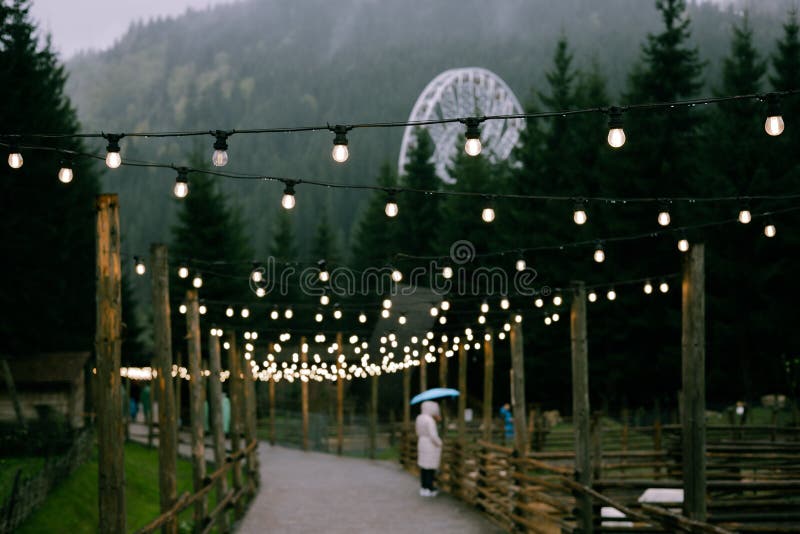 A string lights illuminate a path, leading towards a mountain and a Ferris wheel. A beautiful pathway is illuminated by royalty free stock photography