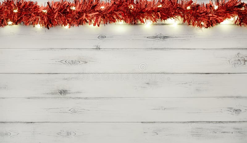 A string of red and silver christmas lights and tinsel, on destressed white wood