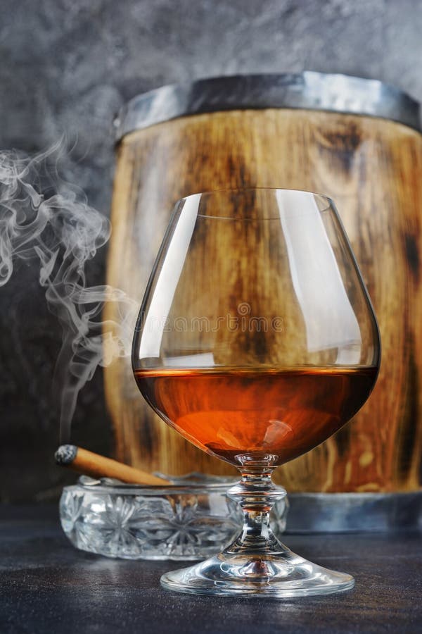 Strong alcoholic drink cognac in sniffer glass with smoking cigar in crystal ashtray and vintage wooden barrel royalty free stock image Strong alcoholic drink cognac in sniffer glass with smoking cigar in crystal ashtray and vintage wooden barrel royalty free stock image