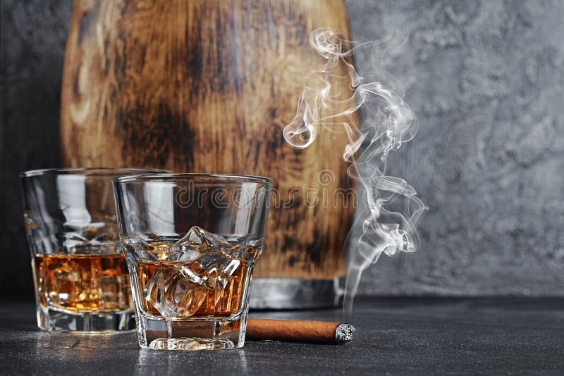 Strong alcoholic drink scotch whisky with ice cubes in old fashion glasses with smoking cigar and vintage wooden barrel in cellar royalty free stock image Strong alcoholic drink scotch whisky with ice cubes in old fashion glasses with smoking cigar and vintage wooden barrel in cellar royalty free stock image