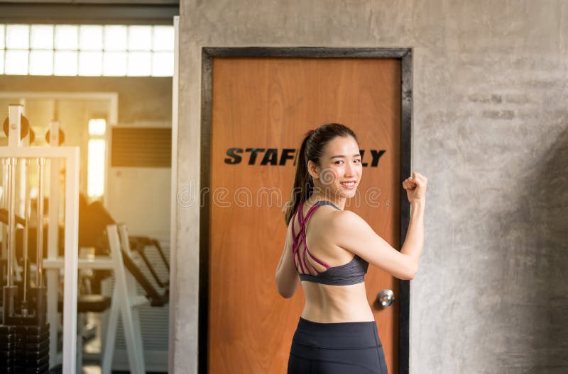 Strong asian woman posture standing and lifting up her arms and exercises muscle at gym