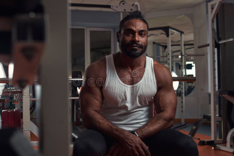 A Strong Athletic Man Sits in the Gym on the Simulator Stock Photo