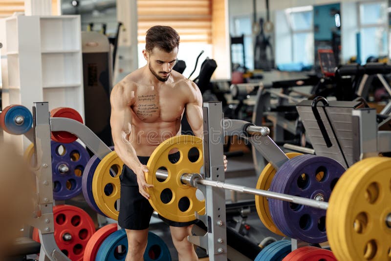 Strong athletic young man bodybuilder fitness model put weights on barbell on the bench in gym. stock image Strong athletic young man bodybuilder fitness model put weights on barbell on the bench in gym. stock image