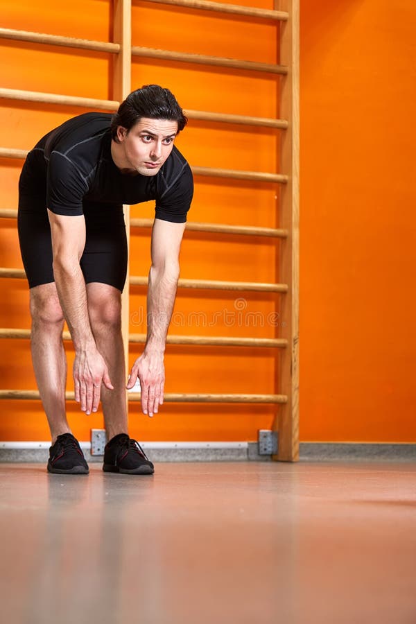 Strong man in the black sportwear stretching arms before gym workout against bright orange wall. stock image Strong man in the black sportwear stretching arms before gym workout against bright orange wall. stock image