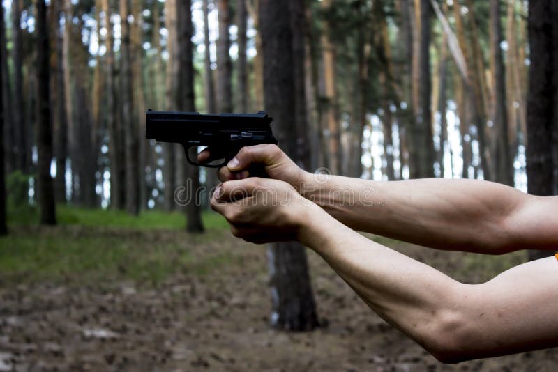 Strong Men`s Hands Hold a Gun Against Forest Background. Danger