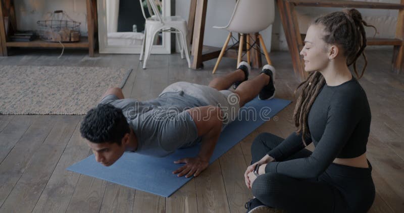 Strong Middle Eastern man doing push-up exercise while Caucasian girlfriend supporting during practice at home stock video footage