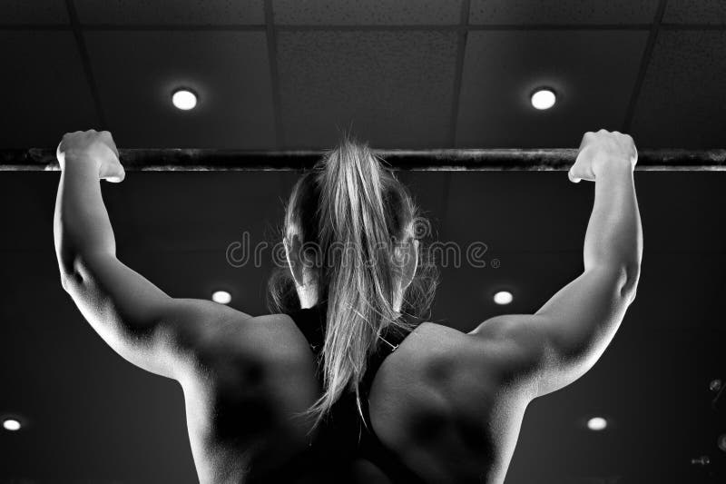 Strong muscular female doing pull up in gym