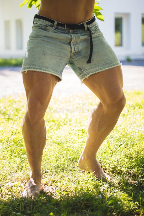 Strong thick legs men bodybuilder in Jean shorts in summer park. 