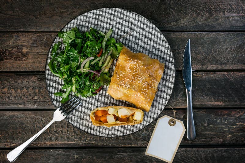 Strudel con la zucca, il feta e l'insalata di verdure, serviti sul piatto ceramico con la coltelleria fotografia stock libera da diritti Strudel con la zucca, il feta e l'insalata di verdure, serviti sul piatto ceramico con la coltelleria fotografia stock libera da diritti