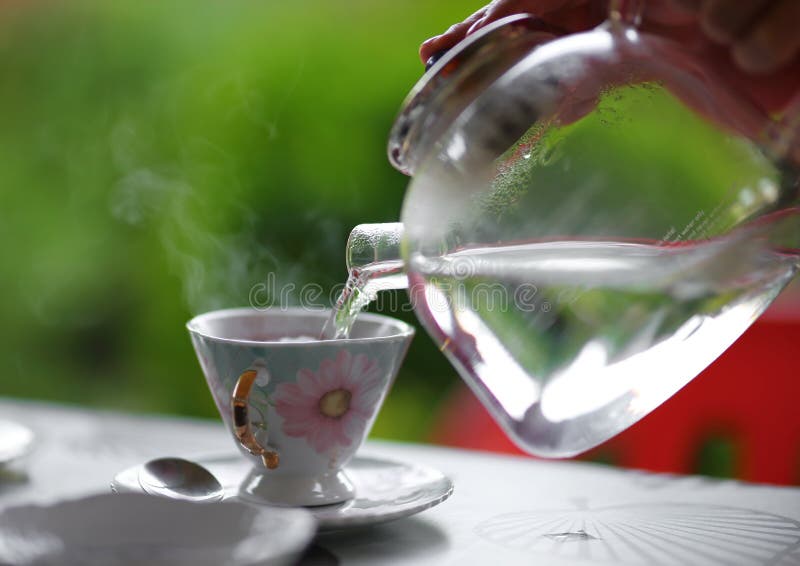 Strömendes Heißwasser von der Glasteekanne in die Teeschale, Sommer im Freien lizenzfreie stockfotografie Strömendes Heißwasser von der Glasteekanne in die Teeschale, Sommer im Freien lizenzfreie stockfotografie