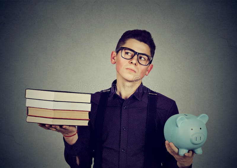 Student loan concept. Young man with stack pile of books and piggy bank full of debt rethinking future career path. Student loan concept. Young man with stack pile of books and piggy bank full of debt rethinking future career path