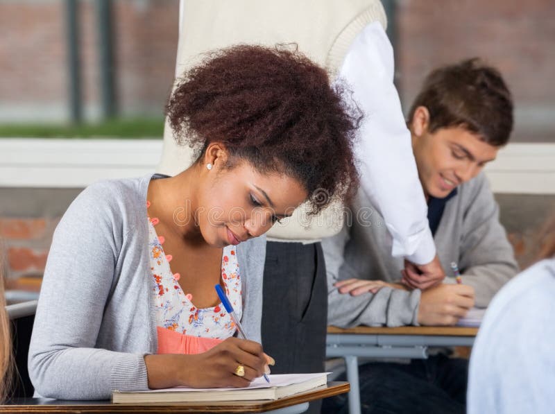 Studencki Writing egzamin Podczas gdy nauczyciela Wyjaśniać zdjęcia stock Studencki Writing egzamin Podczas gdy nauczyciela Wyjaśniać zdjęcia stock