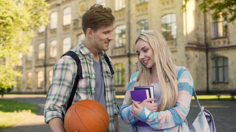 Student, der den Ball, flirtend mit hübschem Mädchen nahe der Universität hält und bitten um Datum stockfotos Student, der den Ball, flirtend mit hübschem Mädchen nahe der Universität hält und bitten um Datum stockfotos