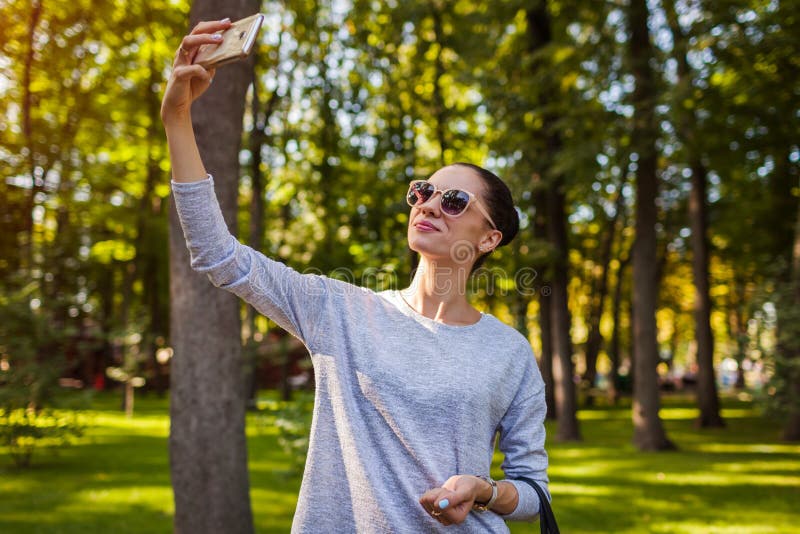 Student die selfie op mobiele telefoon in park nemen Jonge vrouw die zonnebril draagt stock fotografie Student die selfie op mobiele telefoon in park nemen Jonge vrouw die zonnebril draagt stock fotografie