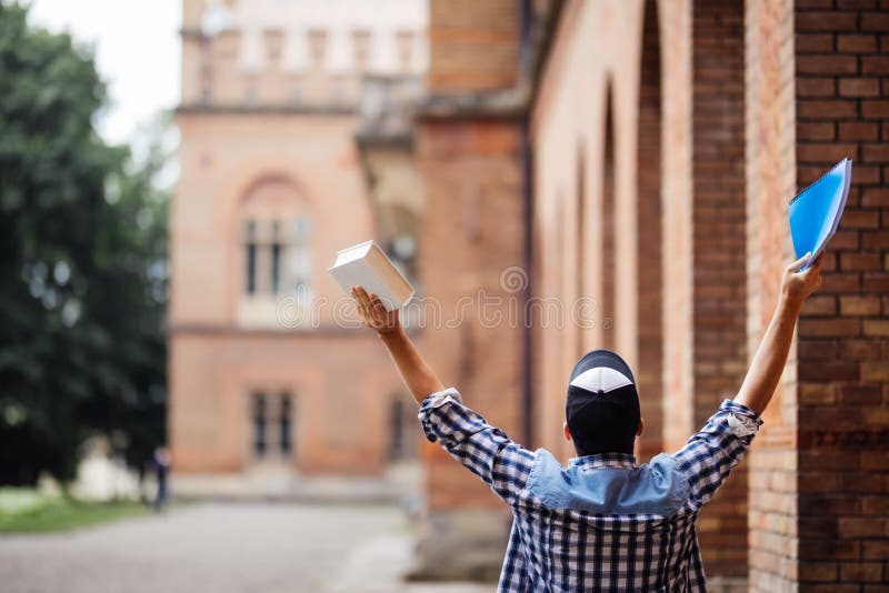 Student för ung man med lyftta händer av framgång framme av Uni universitetsområdet Happuseger för ung man av passerandeexamen St arkivfoto Student för ung man med lyftta händer av framgång framme av Uni universitetsområdet Happuseger för ung man av passerandeexamen St arkivfoto