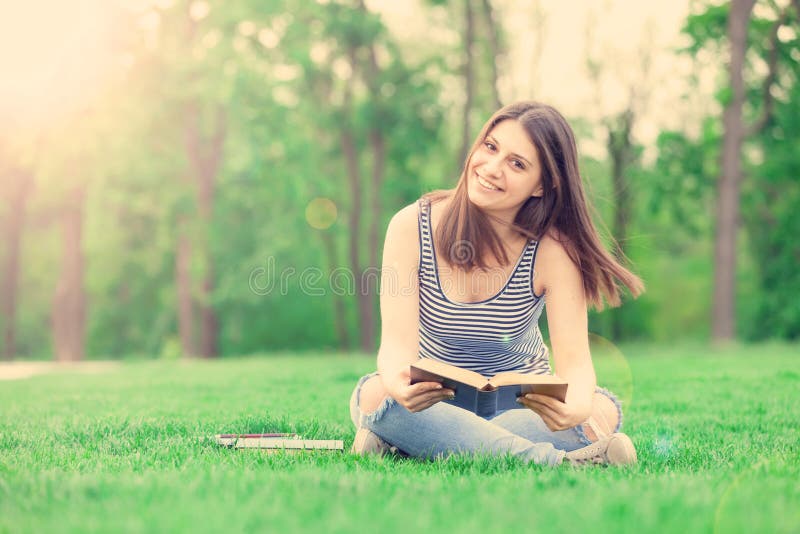 Ritratto di una bella bruna ragazza studente con libri sull'erba verde nel parco in primavera.