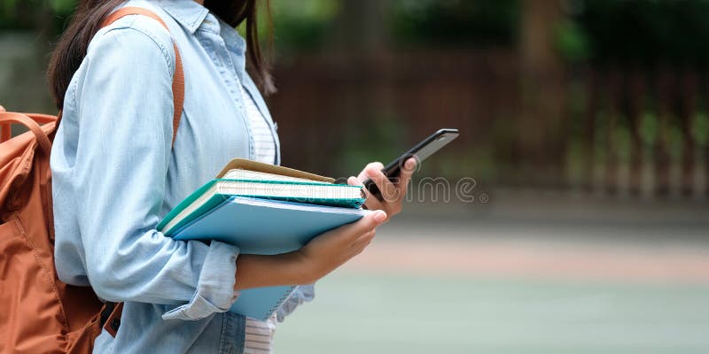 Student girl holding books and smartphone while walking in school campus background, education, back to school concept royalty free stock photo